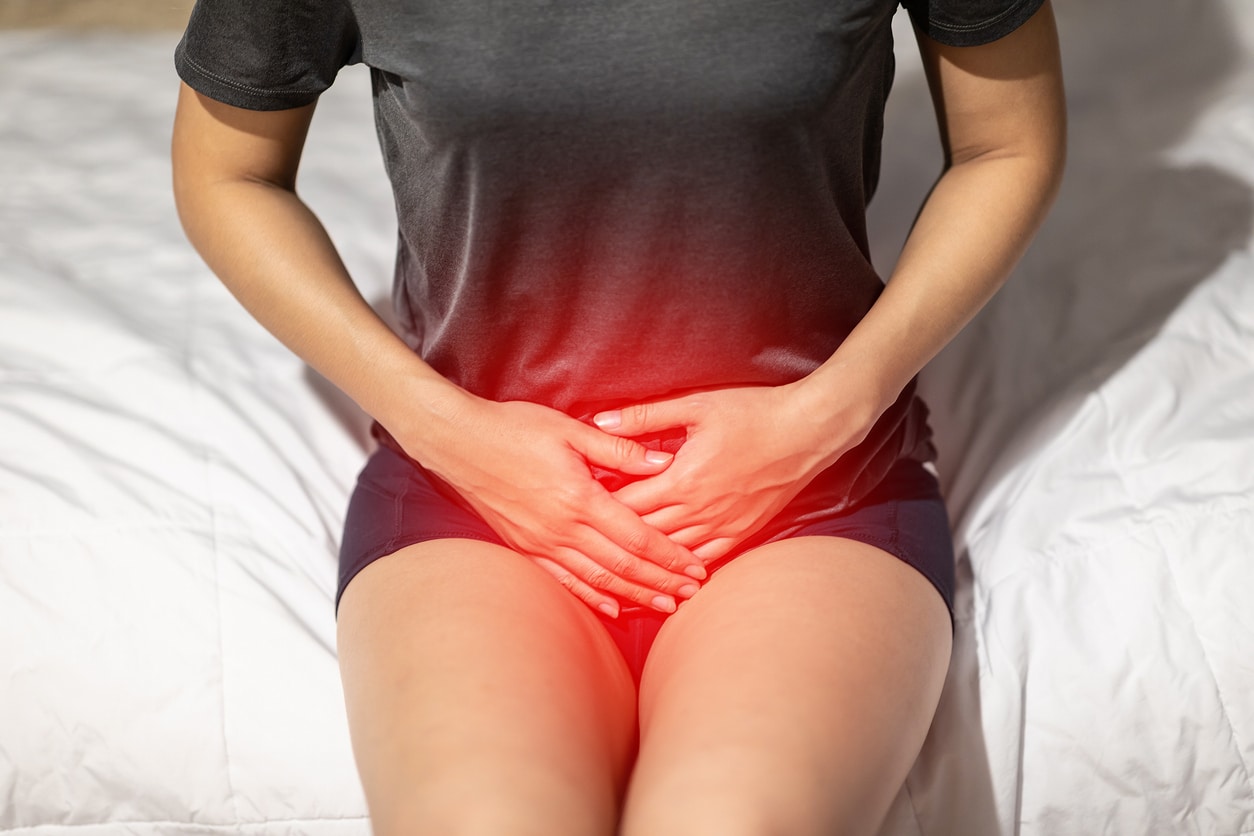 A Woman In A Dark Gray Shirt And Black Shorts Experiencing Pelvic Pain Highlighted In Red.