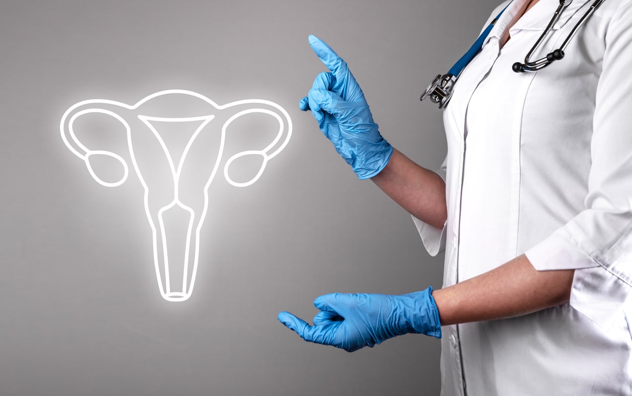 A doctor in a white coat and blue gloves pointing towards a uterus illustration on a gray background.