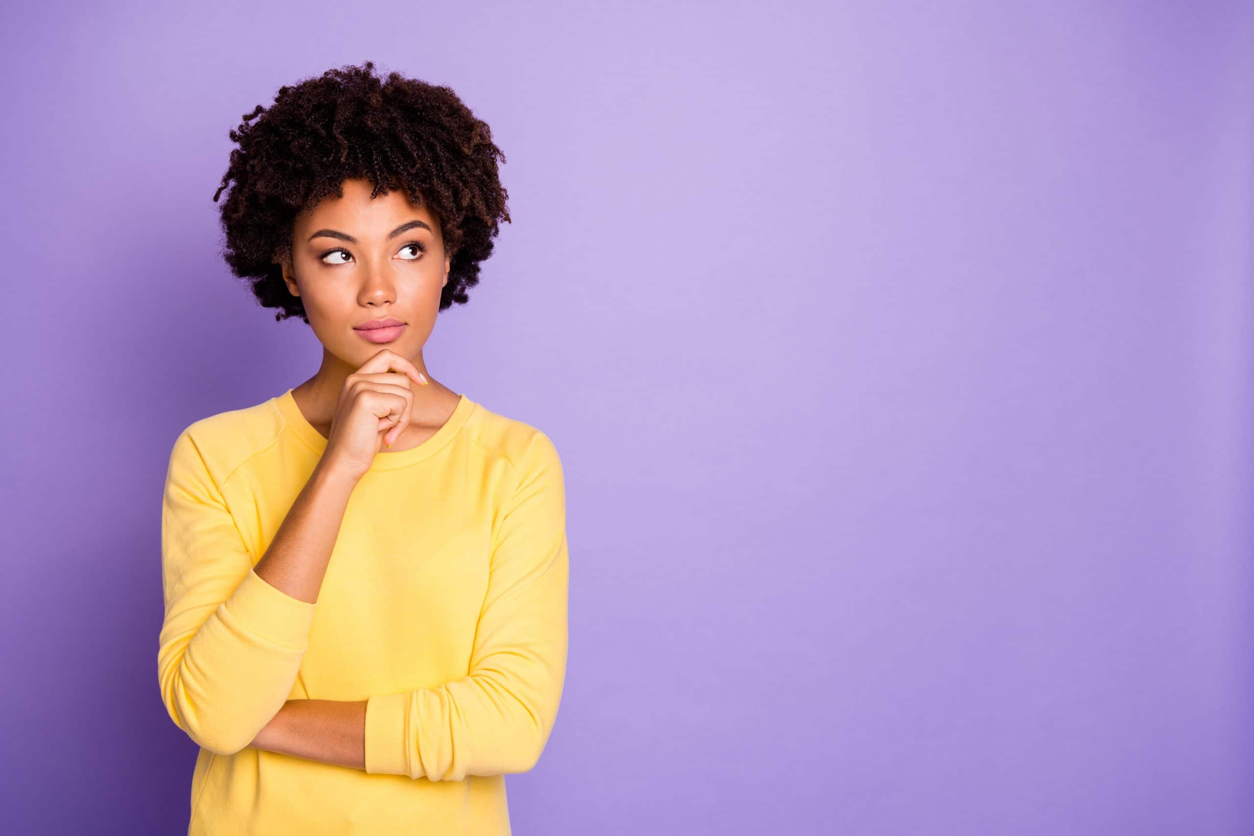 A young woman in a yellow sweater holds her chin, contemplating her endometriosis treatment options