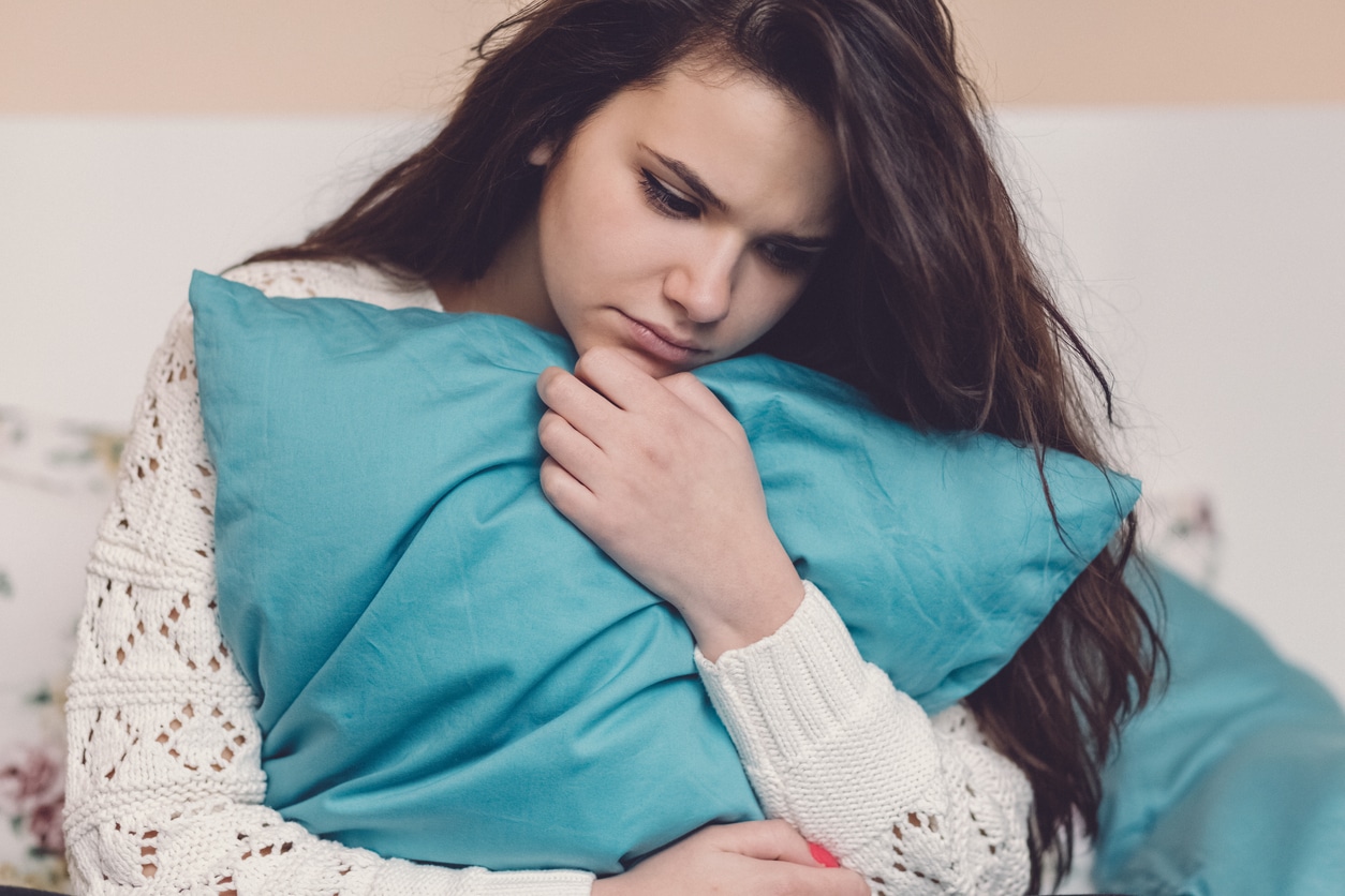 Girl holding a turquoise pillow while looking downcast.