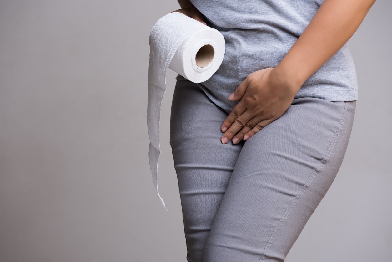 Woman hand holding her lower abdomen and a toilet paper roll.