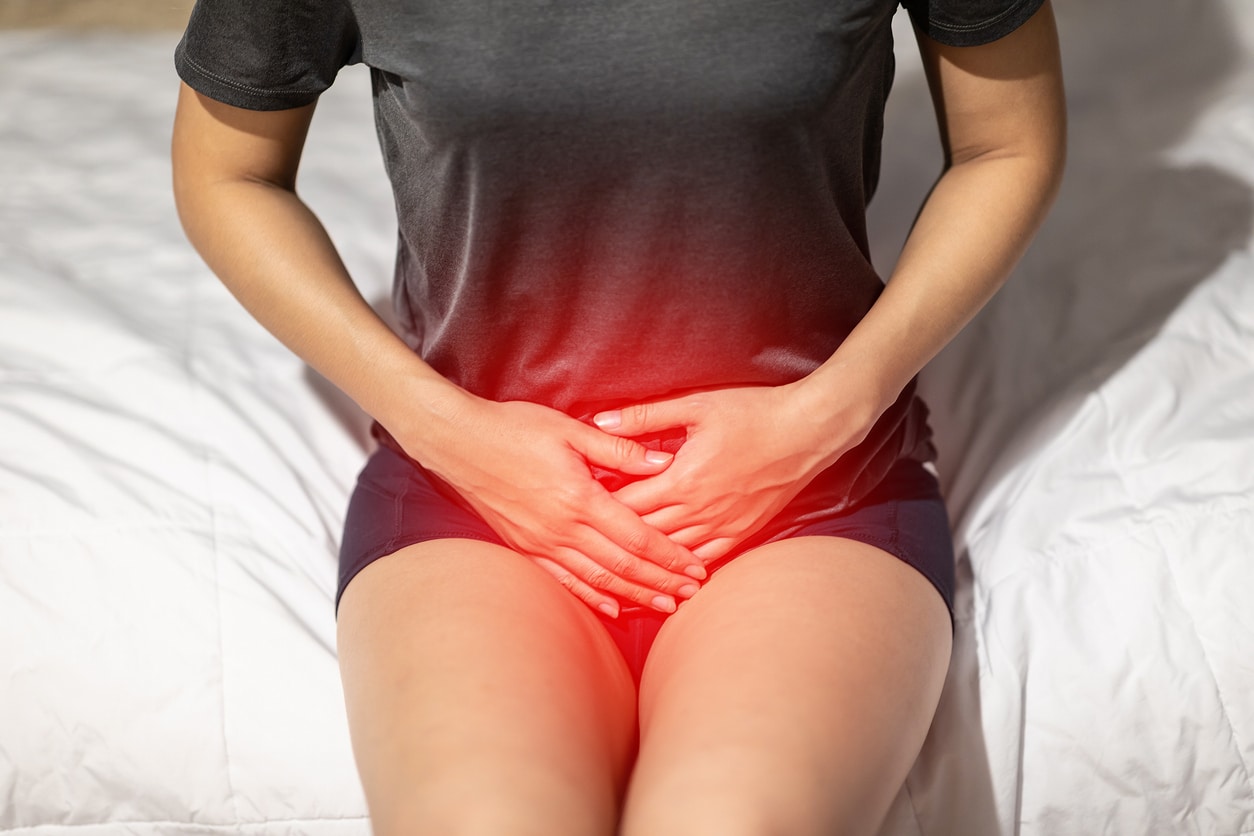 A woman in a dark gray shirt and black shorts experiencing pelvic pain highlighted in red.