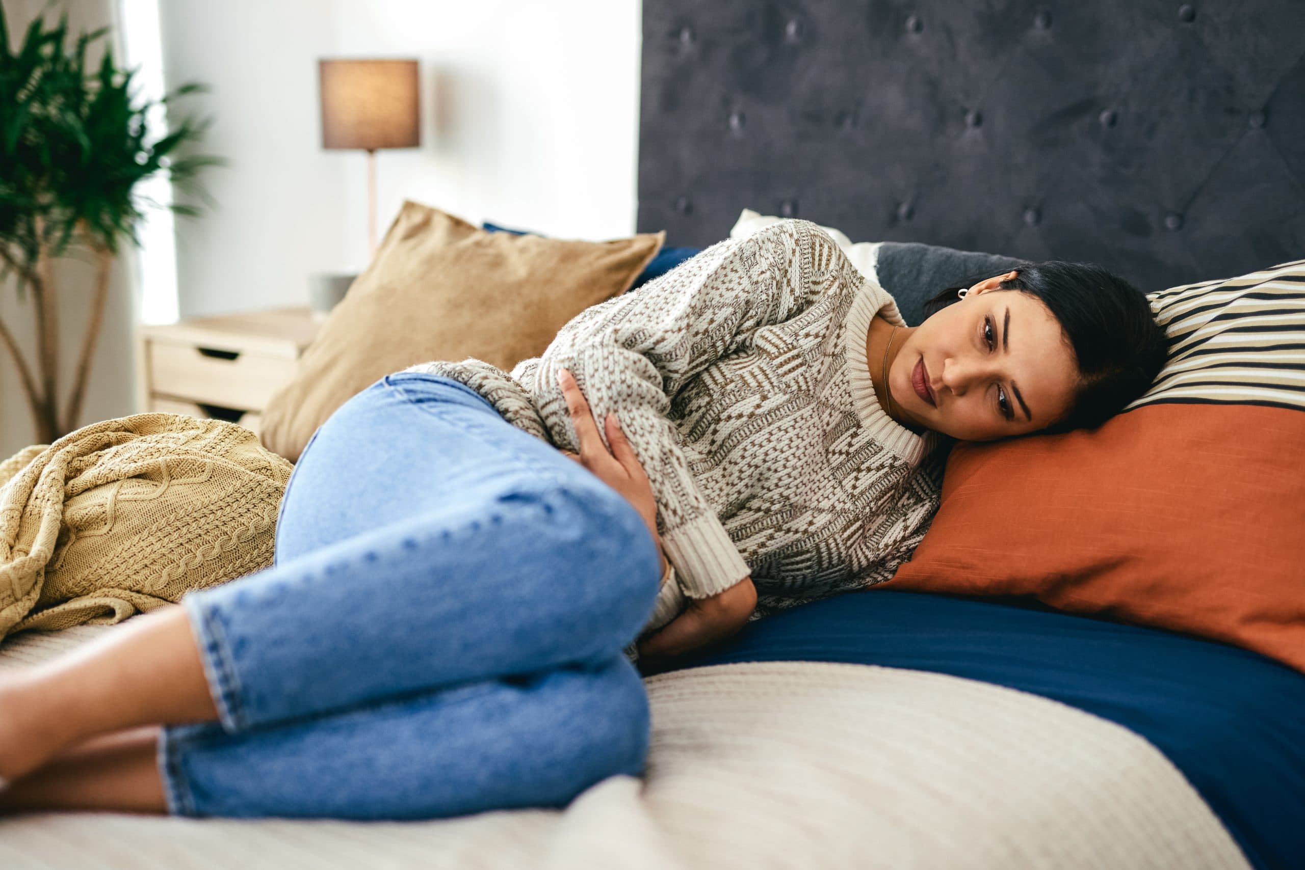 A young woman lying down on a bed and holding her abdomen due to pelvic pain