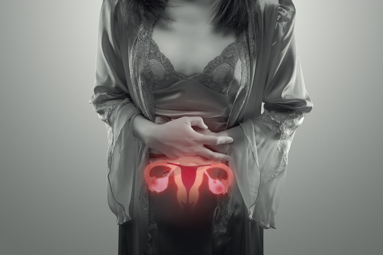 A black and white photo of a woman holding her stomach with a colored uterus illustration.