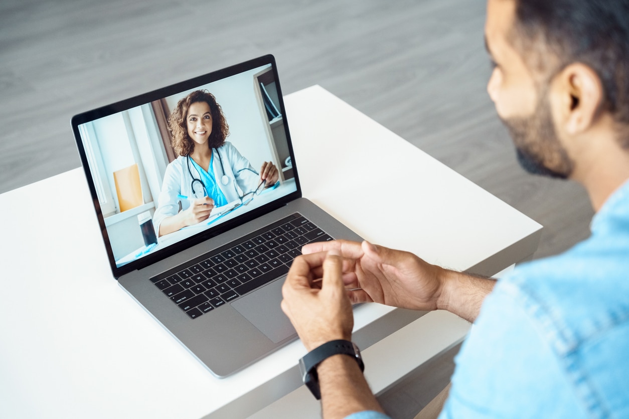 iew over a man’s shoulder sitting at a desk receiving a medical consultation online.