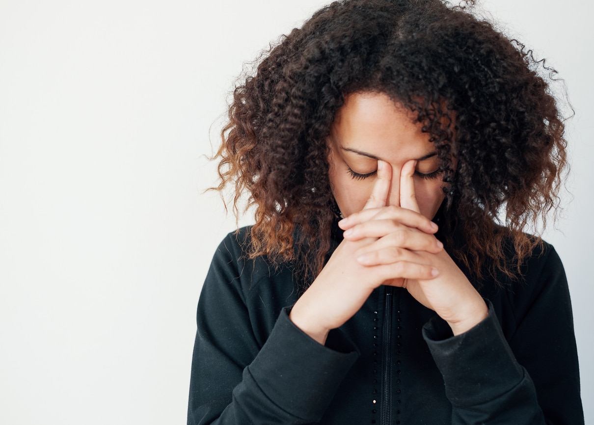 A young woman in a black shirt with her hands in a praying position with fingers in between her eyebrows.
